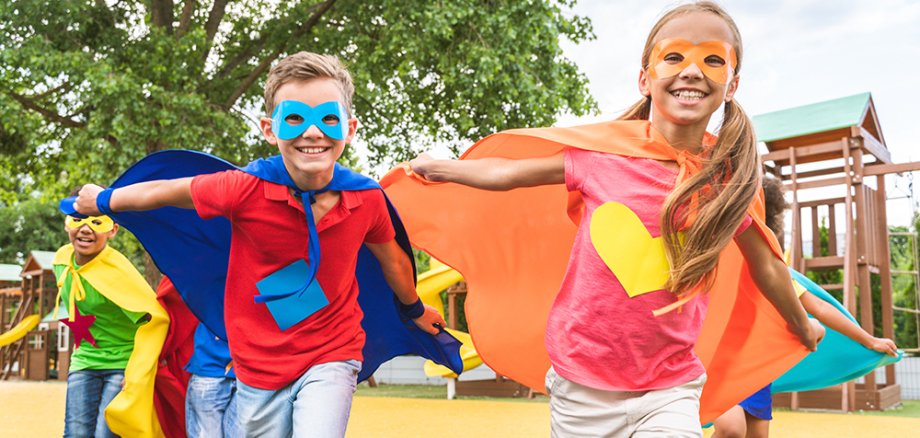 Kinder verkleidet als Superhelden laufen auf dem Spielplatz.