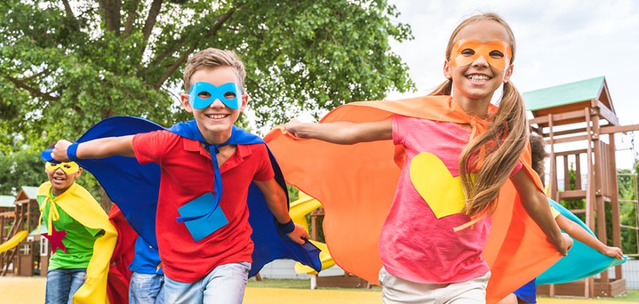 Kinder verkleidet als Superhelden laufen auf dem Spielplatz.