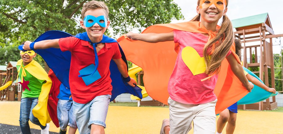 Kinder verkleidet als Superhelden laufen auf dem Spielplatz.