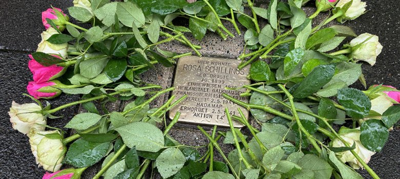 Ein silberner Stein mit Gravur "Rosa Schillings" umringt von rosa Rosen.