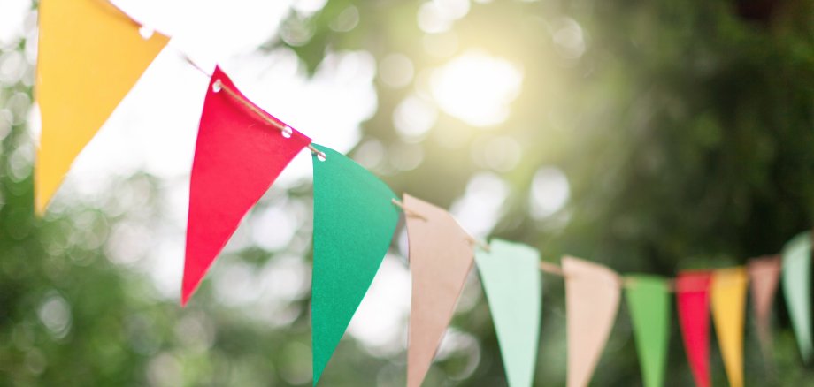 Garland of colorful flags at sunset in summer garden. Concept of celebration Happy Birthday party. Paper festive decoration outdoor.