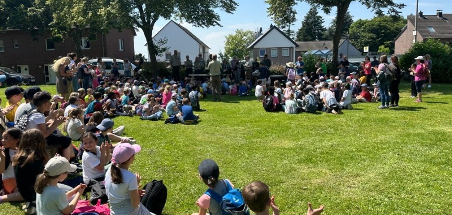 Viele Kinder sitzen auf einer Wiese im Kreis.