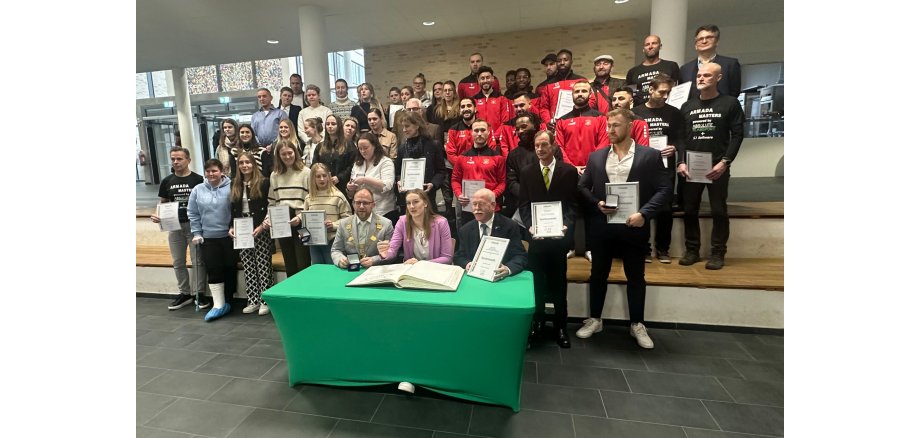 Viele Sportler hinter einem Tisch mit dem Goldenen Buch Stadt Würselen und Bürgermeister Nießen