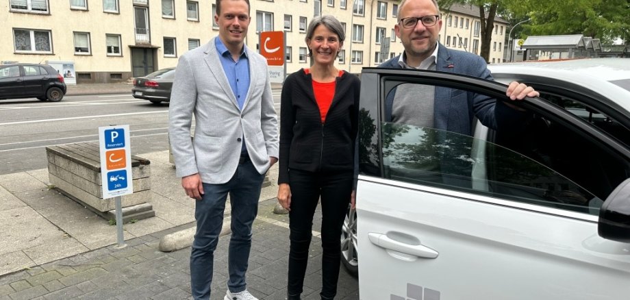 Bürgermeister Roger Nießen und Planungsamtsleiter Benjamin Gard stehen an einem Cambio Auto auf einem Cambio Stellplatz.