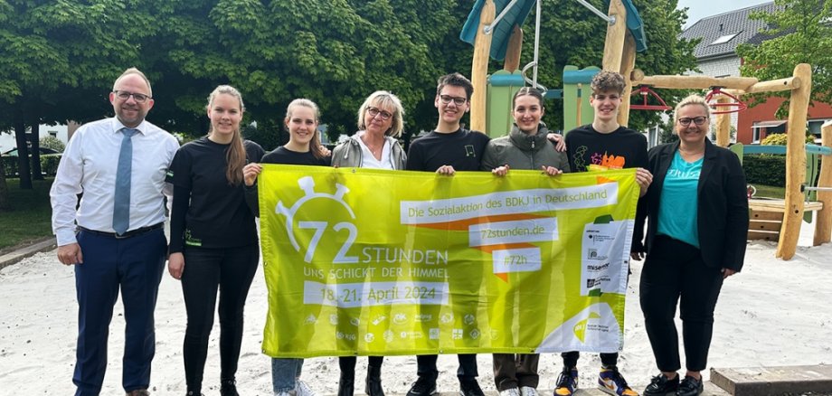 Bürgermeister Roger Nießen und die Mitarbeiterin vom Baubetriebshof stehen vor dem Spielplatz mit den Kindern, die mit an der AKtion gearbeitet haben.