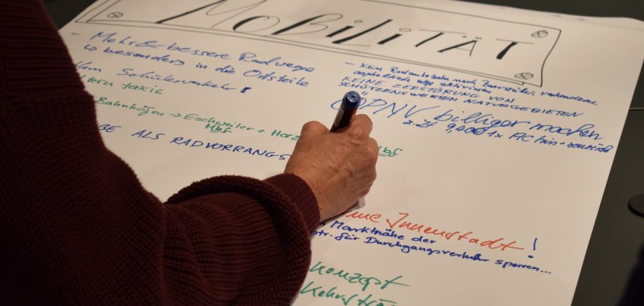 Eine Person schreibt mit einem Stift auf ein großes Plakat.