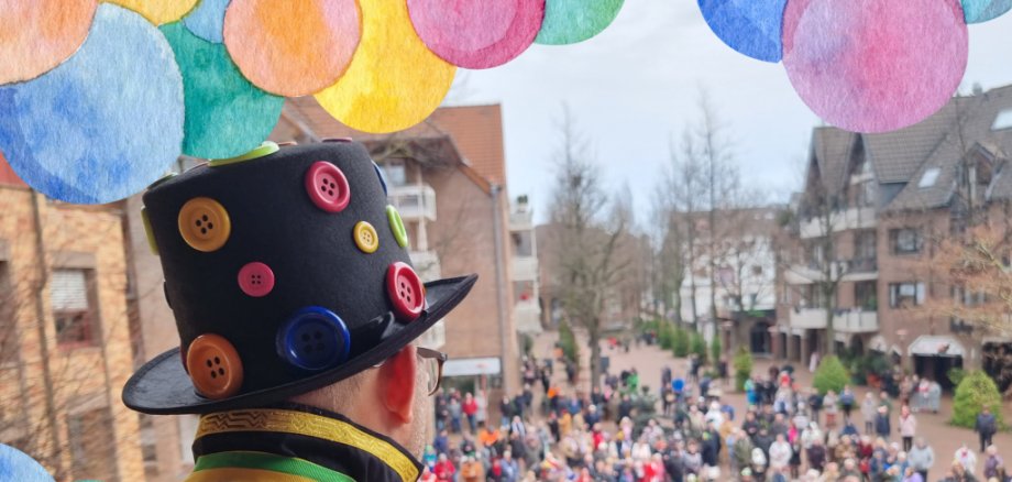 Blick über die Schulter vom Bürgermeister, der als Clown verkleidet ist und auf dem Balkon des RFathauses steht. Viele Karnevalisten sind auf dem Morlaixplatz versammelt.